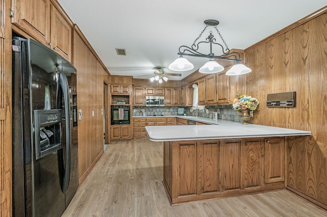 613 Bennett Dr, Dumas, TX 79029 - kitchen featuring black appliances, brown cabinets, a peninsula, wooden walls, and light wood-style floors