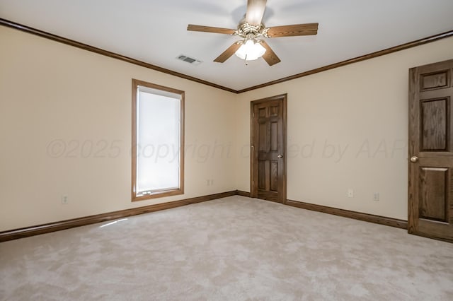 carpeted spare room featuring a ceiling fan, visible vents, crown molding, and baseboards