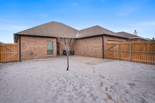 rear view of house featuring a patio, brick siding, a shingled roof, fence, and a gate