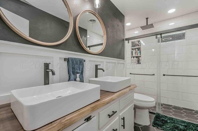 15 Fannin Dr, Tulia, TX 79088 - bathroom with a tile shower, double vanity, toilet, a wainscoted wall, and a decorative wall