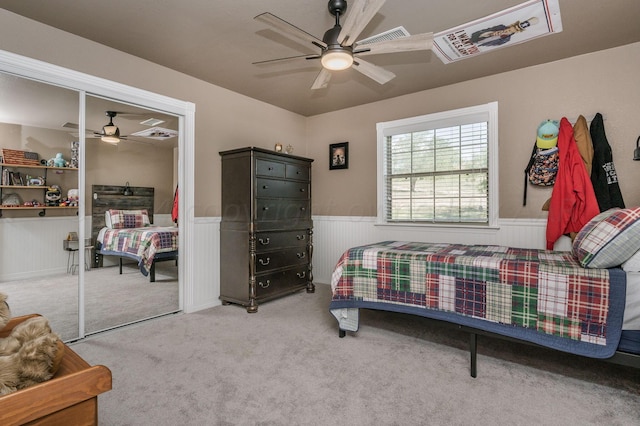 carpeted bedroom featuring a ceiling fan, visible vents, wainscoting, and a closet