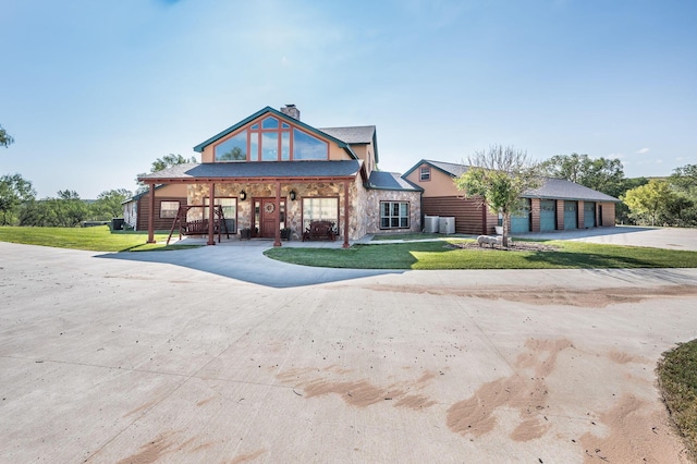 view of front of house featuring covered porch, stone siding, a front yard, curved driveway, and a chimney