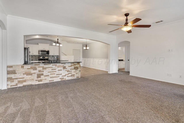 9909 Asher Ave, Amarillo, TX 79119 - unfurnished living room with arched walkways, crown molding, ceiling fan, carpet, and a decorative wall