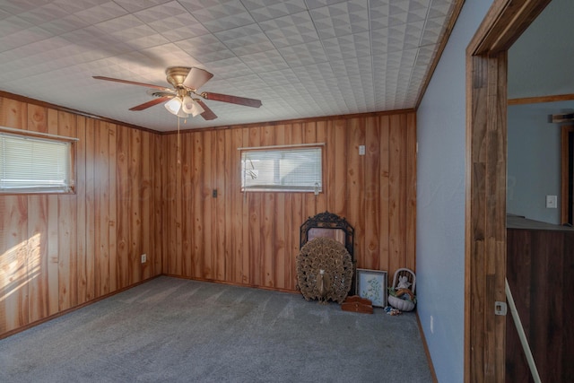 carpeted spare room featuring crown molding, ceiling fan, and wood walls