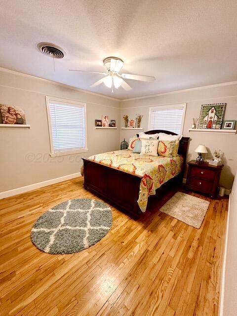 bedroom featuring baseboards, visible vents, a ceiling fan, wood finished floors, and a textured ceiling