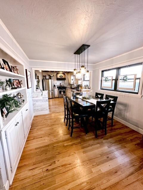 dining space featuring built in shelves, crown molding, light wood-style floors, a textured ceiling, and baseboards