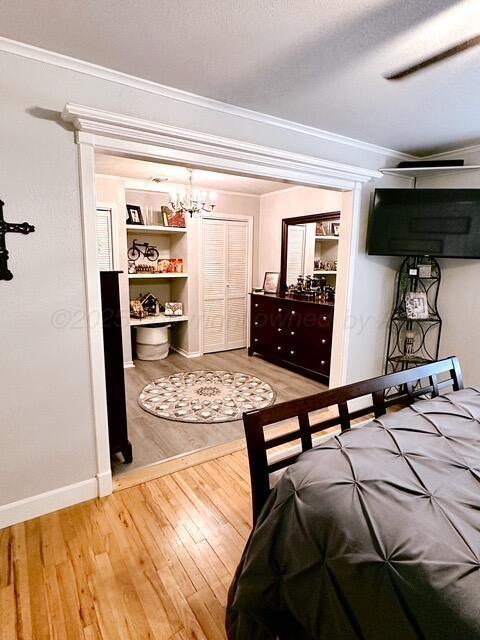 bedroom featuring crown molding, baseboards, wood finished floors, and ceiling fan with notable chandelier