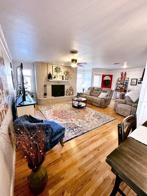 living area with a ceiling fan, a brick fireplace, a textured ceiling, and wood finished floors