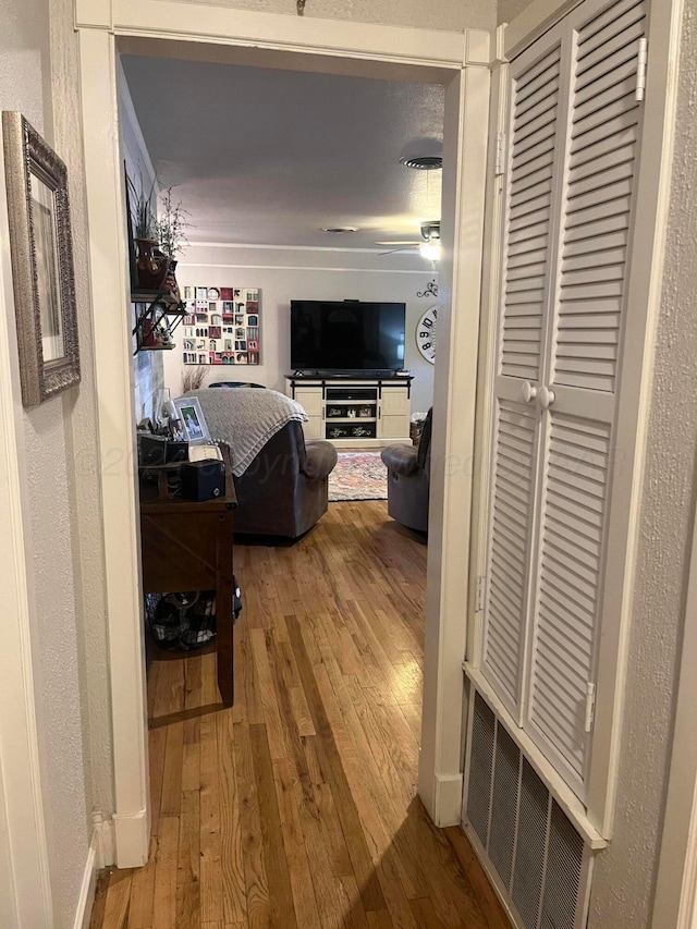 corridor featuring visible vents, a textured wall, baseboards, and wood finished floors