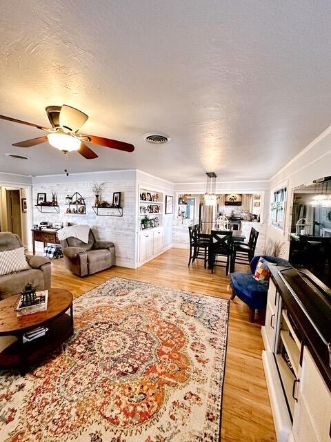 living area featuring a textured ceiling, light wood finished floors, visible vents, and a ceiling fan