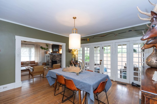 dining area with french doors, crown molding, wood finished floors, and a fireplace