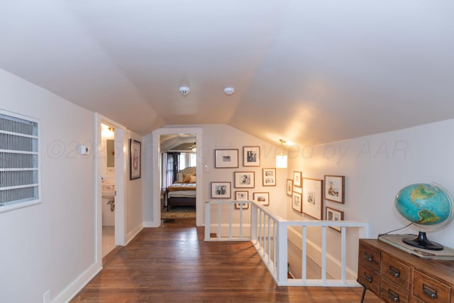 corridor featuring dark wood finished floors, lofted ceiling, baseboards, and an upstairs landing
