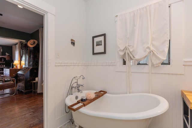 bathroom with wood finished floors, a freestanding tub, wainscoting, and a decorative wall