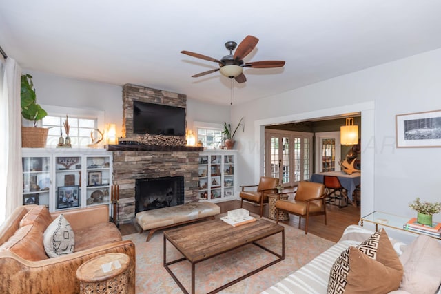 living room featuring ceiling fan, a stone fireplace, wood finished floors, and healthy amount of natural light