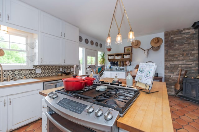kitchen featuring stainless steel range with gas stovetop, butcher block counters, white cabinetry, a wood stove, and a sink