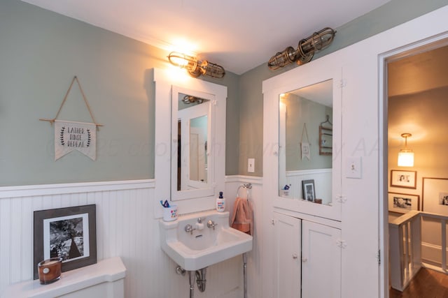 half bath with wainscoting, toilet, and a sink