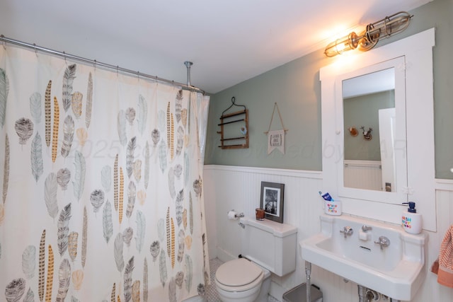 bathroom with wainscoting, toilet, curtained shower, and a sink