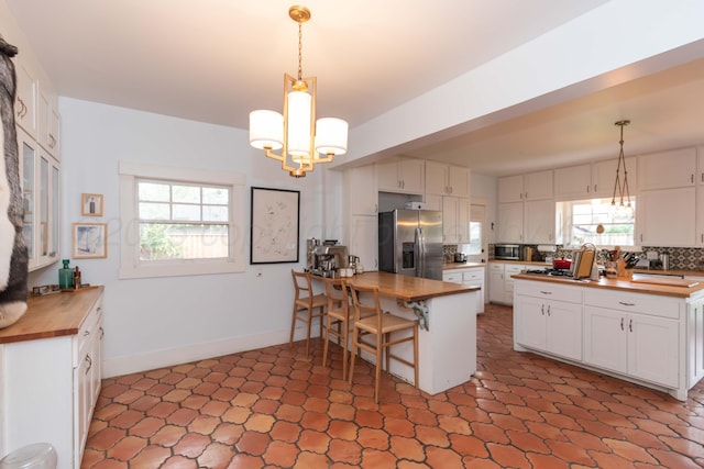 kitchen featuring butcher block counters, appliances with stainless steel finishes, a chandelier, white cabinetry, and tasteful backsplash