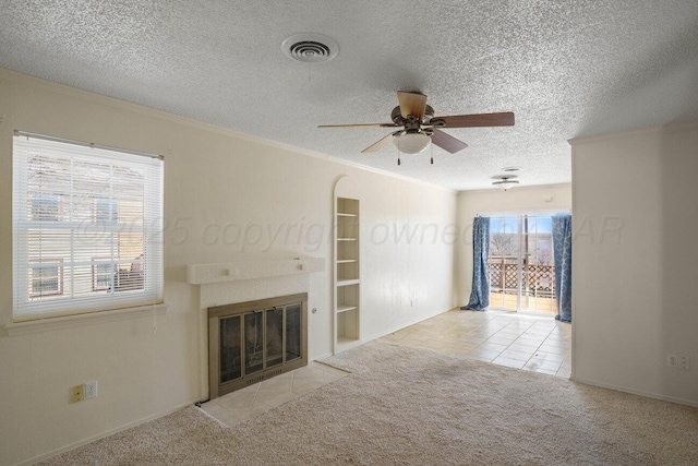 unfurnished living room with carpet flooring, a textured ceiling, ceiling fan, crown molding, and a fireplace