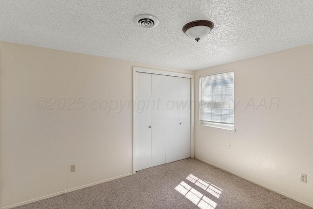 unfurnished bedroom featuring light carpet, a textured ceiling, baseboards, visible vents, and a closet