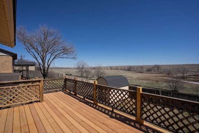 wooden deck with an outdoor structure, fence, a rural view, and a storage unit