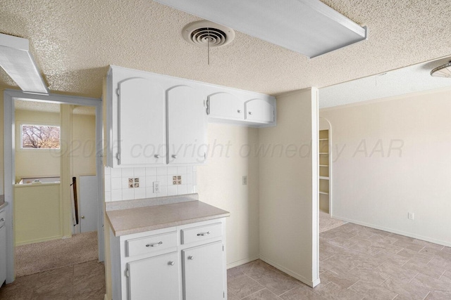 kitchen with a textured ceiling, tasteful backsplash, visible vents, white cabinetry, and light countertops