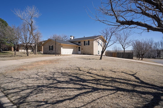 view of front facade with brick siding, an attached garage, a chimney, and driveway