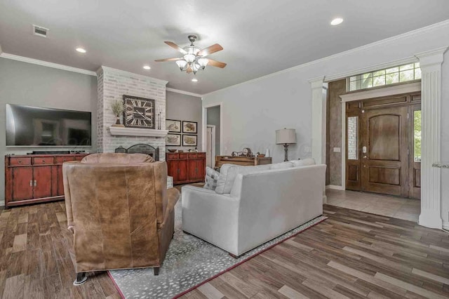 living room with a ceiling fan, wood finished floors, a brick fireplace, ornamental molding, and recessed lighting