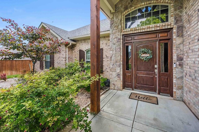 entrance to property featuring a shingled roof, brick siding, and fence