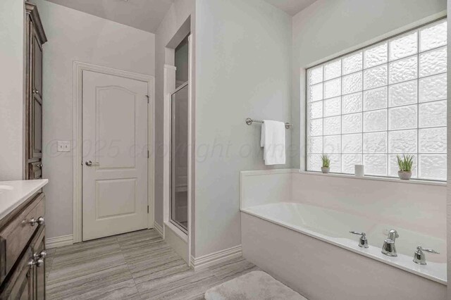 bathroom featuring healthy amount of natural light, baseboards, a stall shower, and vanity