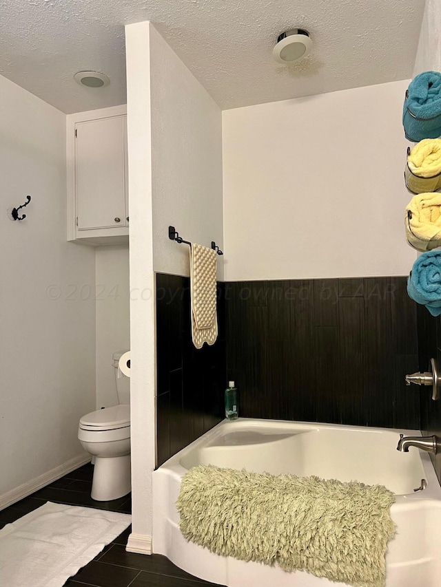 bathroom with toilet, a tub to relax in, a textured ceiling, and tile patterned floors