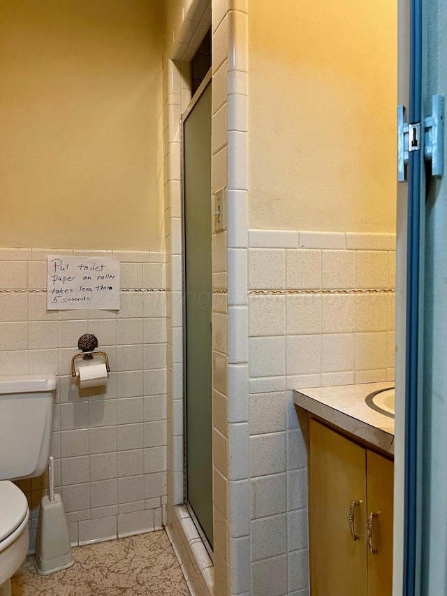 bathroom with tile walls, an enclosed shower, vanity, and toilet