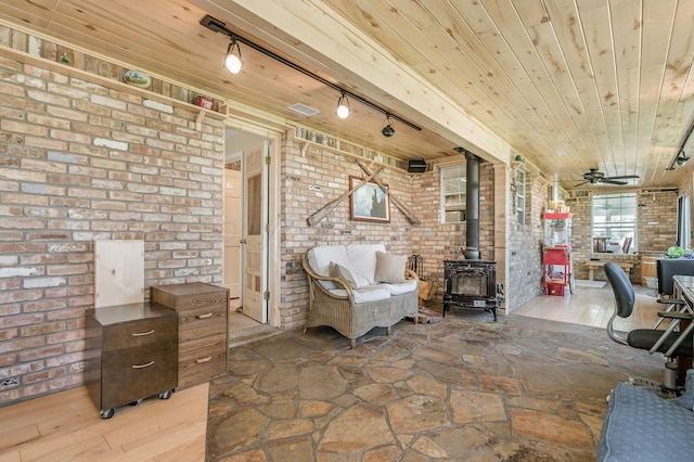 sitting room with rail lighting, brick wall, ceiling fan, hardwood / wood-style floors, and a wood stove