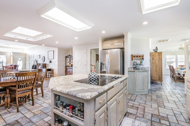 kitchen with light stone countertops, stainless steel fridge, a skylight, and a kitchen island