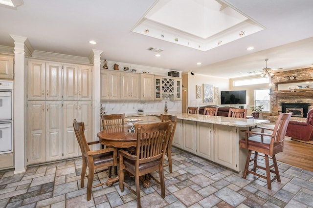 kitchen with crown molding, light stone countertops, cream cabinetry, a large fireplace, and a breakfast bar area
