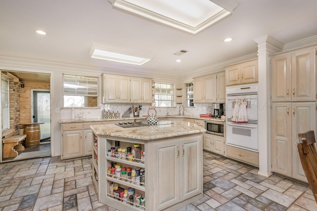 kitchen with light stone countertops, backsplash, black electric cooktop, double oven, and a kitchen island