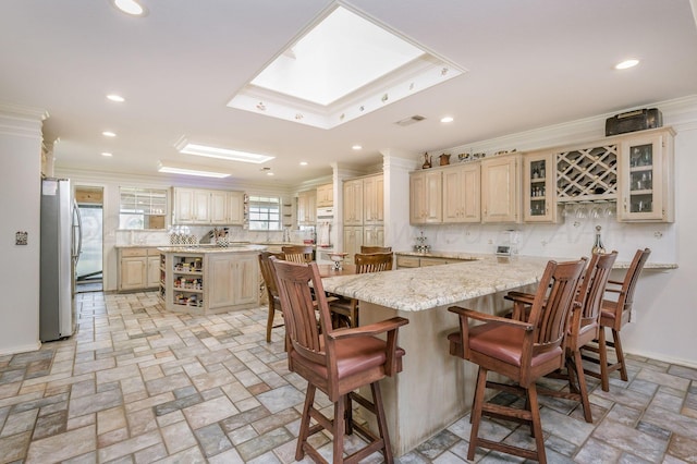 kitchen with a kitchen bar, stainless steel refrigerator, a center island, and ornamental molding