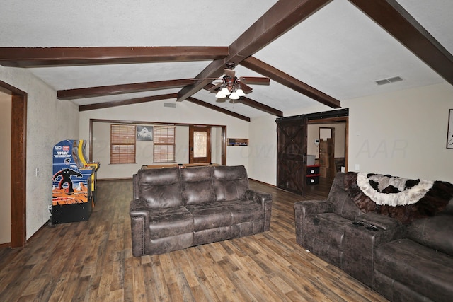 living area featuring a barn door, a ceiling fan, vaulted ceiling with beams, wood finished floors, and visible vents