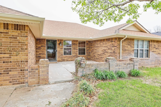 property entrance featuring brick siding, a patio area, and roof with shingles