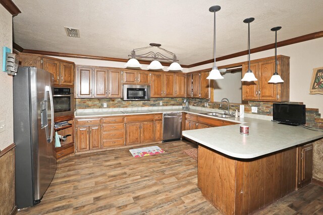 1005 Bennett Dr, Dumas, TX 79029 - kitchen with stainless steel appliances, a sink, a peninsula, light countertops, and brown cabinetry