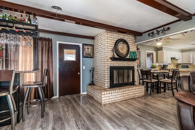 living area with visible vents, ceiling fan, beamed ceiling, wood finished floors, and a fireplace