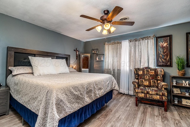 bedroom with a textured ceiling, ceiling fan, wood finished floors, and visible vents