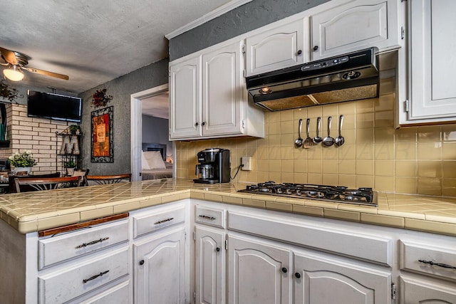 kitchen featuring a peninsula, a ceiling fan, white cabinets, and under cabinet range hood