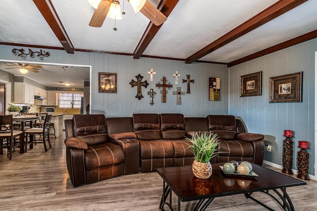 living area with beam ceiling, ceiling fan, and light wood finished floors