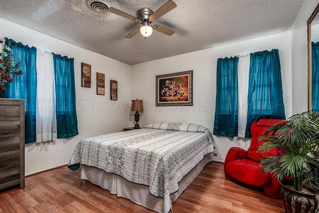 bedroom featuring a ceiling fan, a textured ceiling, visible vents, and wood finished floors