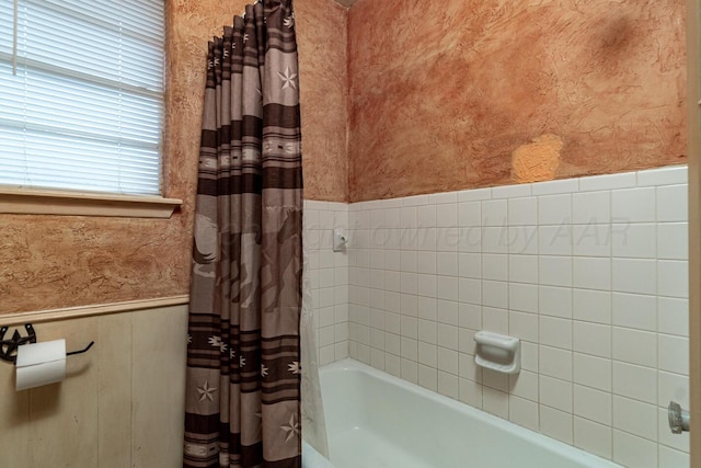 full bath featuring wainscoting, a textured wall, and shower / bathtub combination with curtain