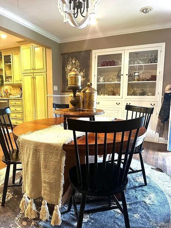 dining area featuring a textured ceiling, a notable chandelier, crown molding, and dark wood-type flooring