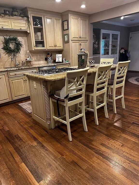 bar featuring dark hardwood / wood-style flooring, backsplash, light stone counters, ornamental molding, and sink