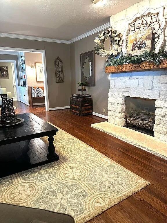 living room featuring a textured ceiling, crown molding, a stone fireplace, and dark wood-type flooring