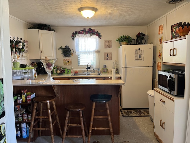 kitchen featuring sink, a breakfast bar, kitchen peninsula, white cabinets, and white fridge